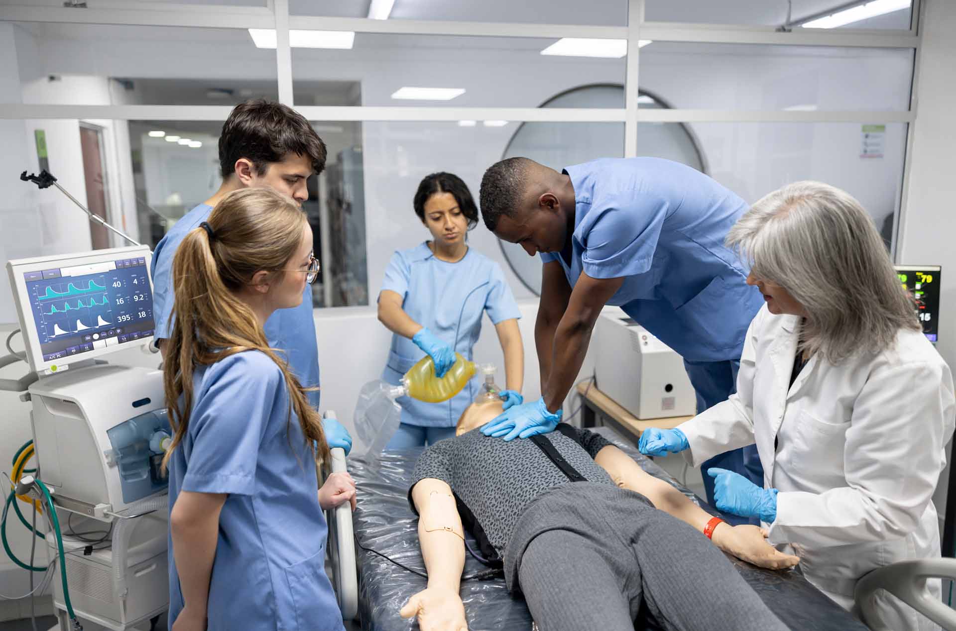 Man in scrubs teaches medical students to perform CPR on a manikin at the hospital.