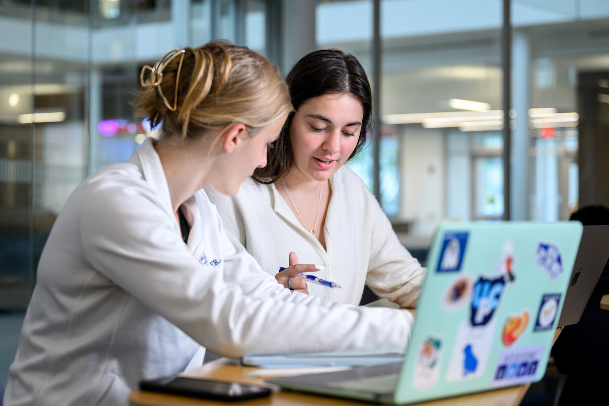 Two Butler students discuss class work while using laptops.