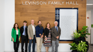 Group of Students, Faculty, and Frank Levinson in front of Levinson Family Hall Plaque