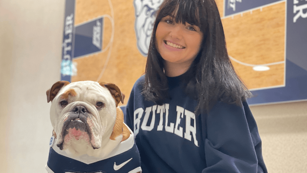 Mascot bulldog in blue jersey, with female student in Butler sweatshirt, long dark hair and bangs