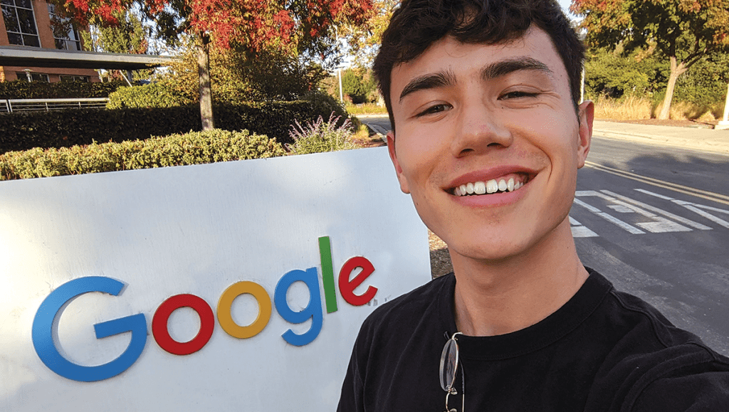 Male with dark short hair, black t-shirt, standing in front of sign that reads Google