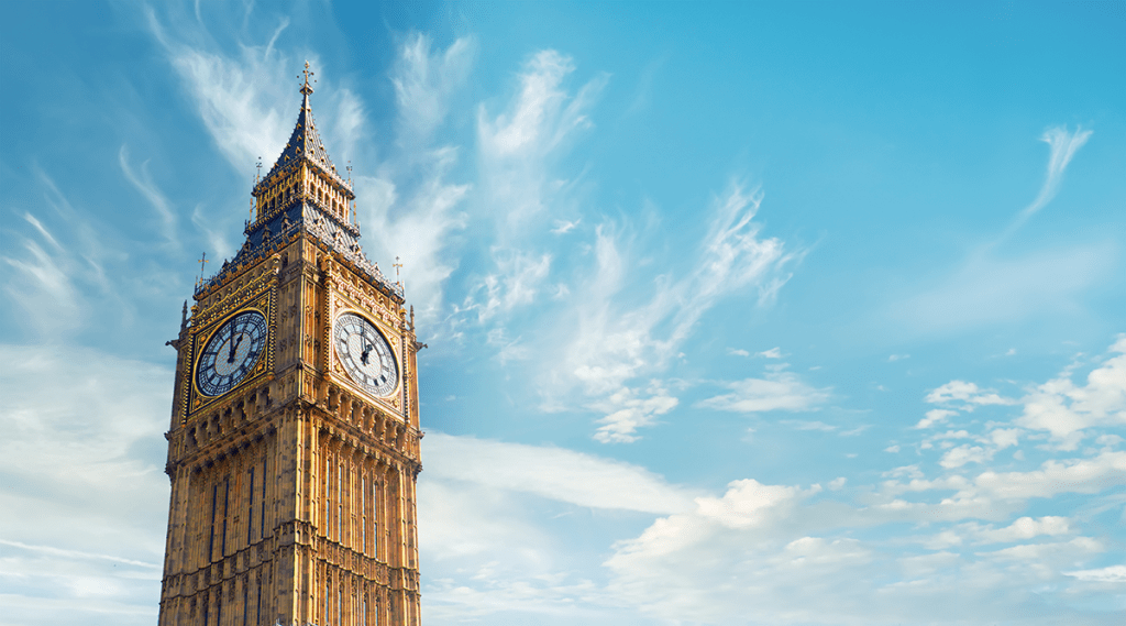 London's Big Ben tower, gold spires with clock reading 1:00, blue sky behind with thin white clouds