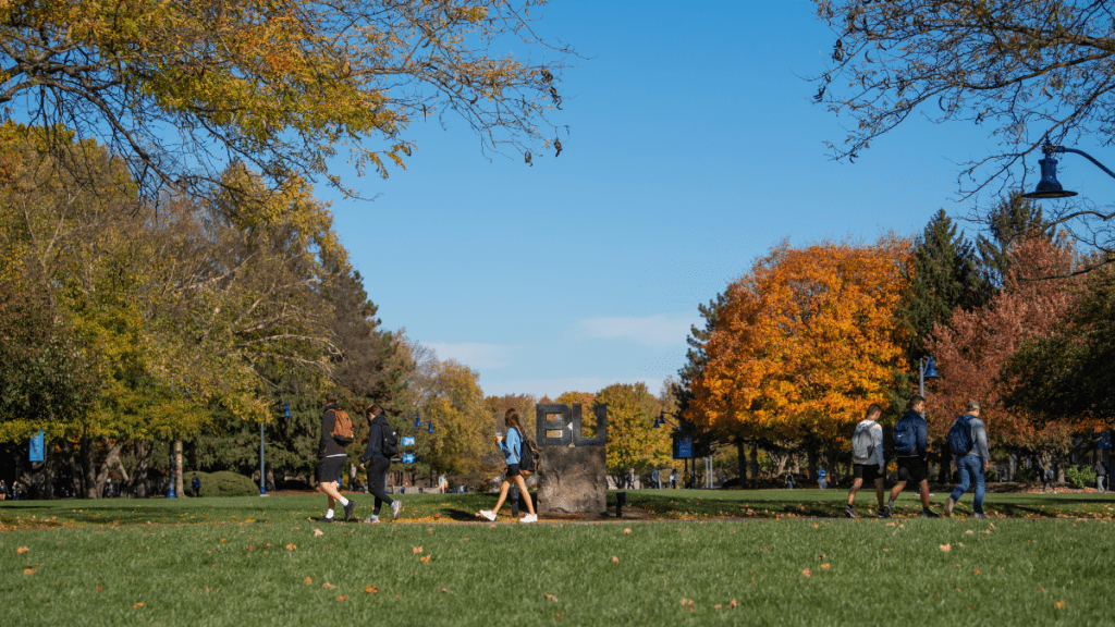Three students walking across a green lawn with fall trees at Butler University