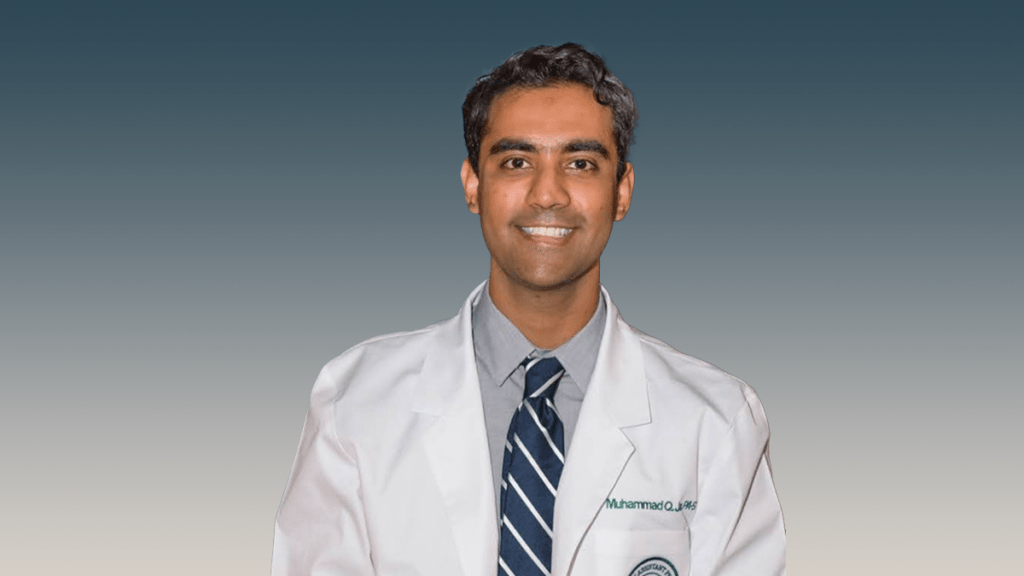 man with light brown hair in white lab coat with blue shirt and dark blue tie with white stripes