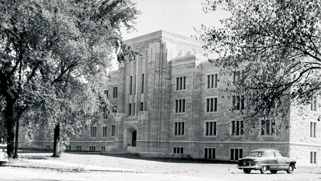 black & white photo of 1955 limestone 4-story building, trees in front, 1955 car parked in front.