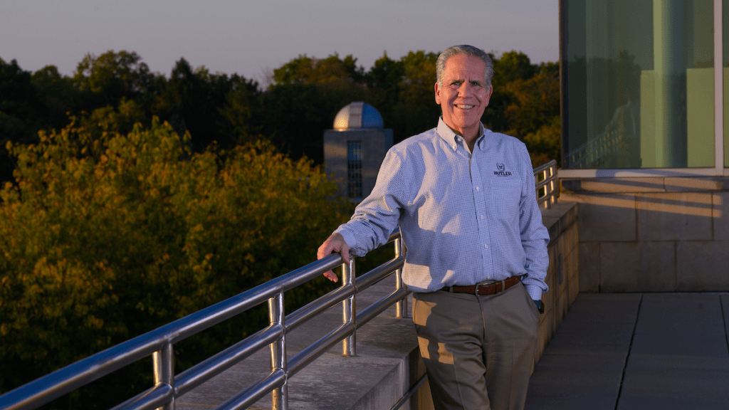 James Danko in blue shirt, tan pants at silver railing with trees and observatory dome behind him