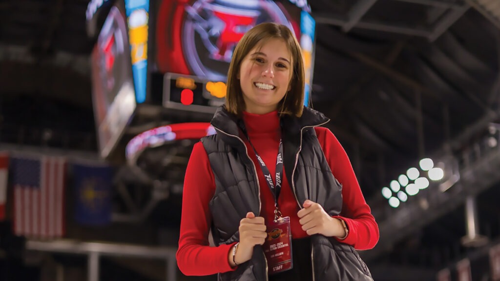 Eva Hallman ’26 wearing a red sweater and black puffer vest, posing in the Indy Fuel arena.