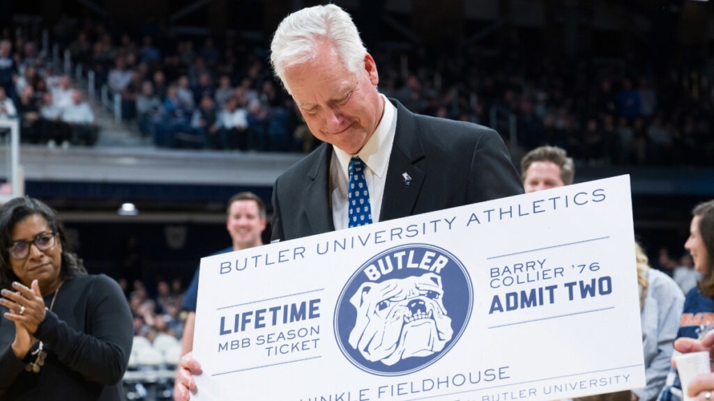 Barry Collier ’76 smiling and looking down at his "Lifetime MBB Season Ticket" that was presented to him on the main court in Hinkle Field House.