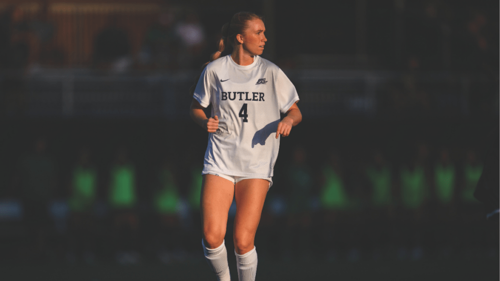 Soccer player, Abby Isger, in a white "BUTLER" jersey with the number "4," running on the field during a game.