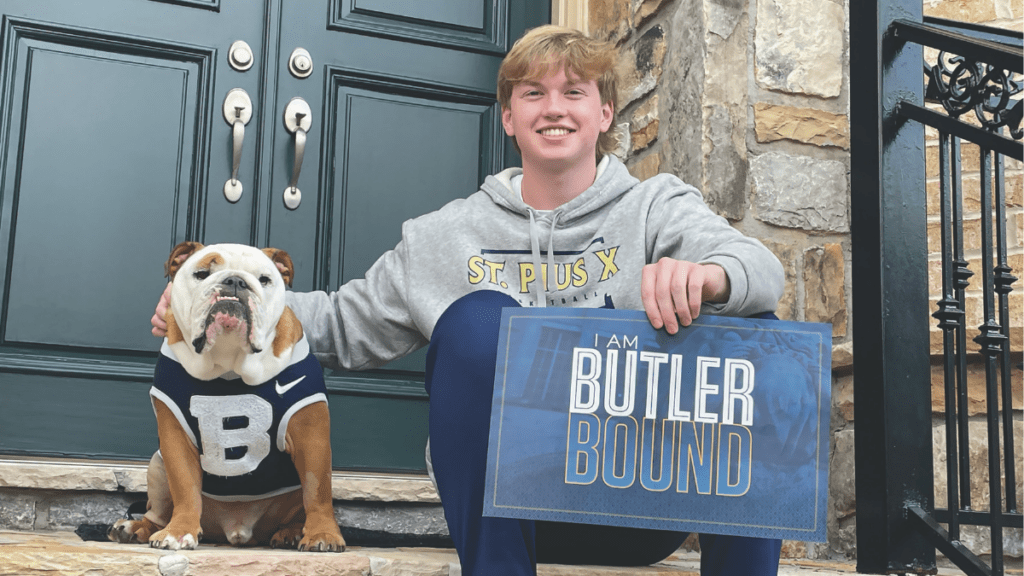 Incoming student sitting on stone steps with Butler Blue IV, holding a sign that says "I AM BUTLER BOUND".