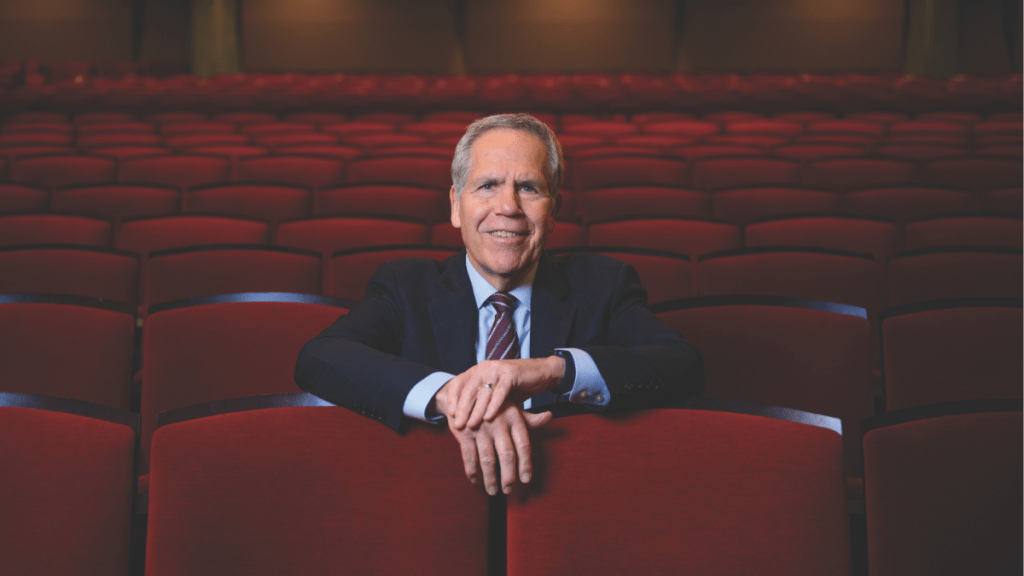 President James Danko leans on a theater seat among rows of red seats.