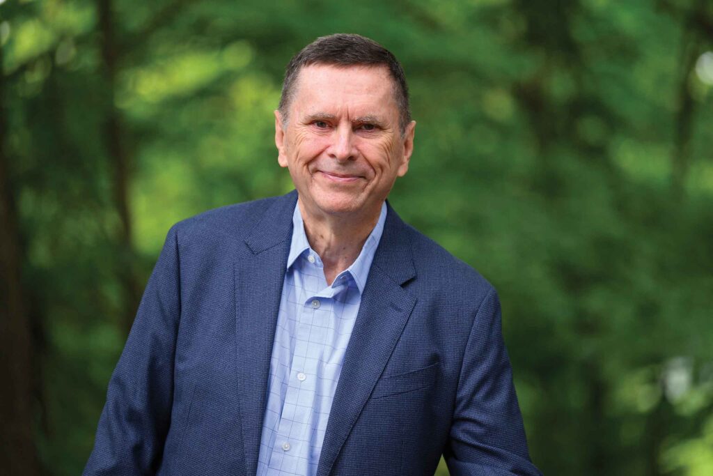 Dan Cooreman in a blue suit jacket smiles in front of a green forest background.