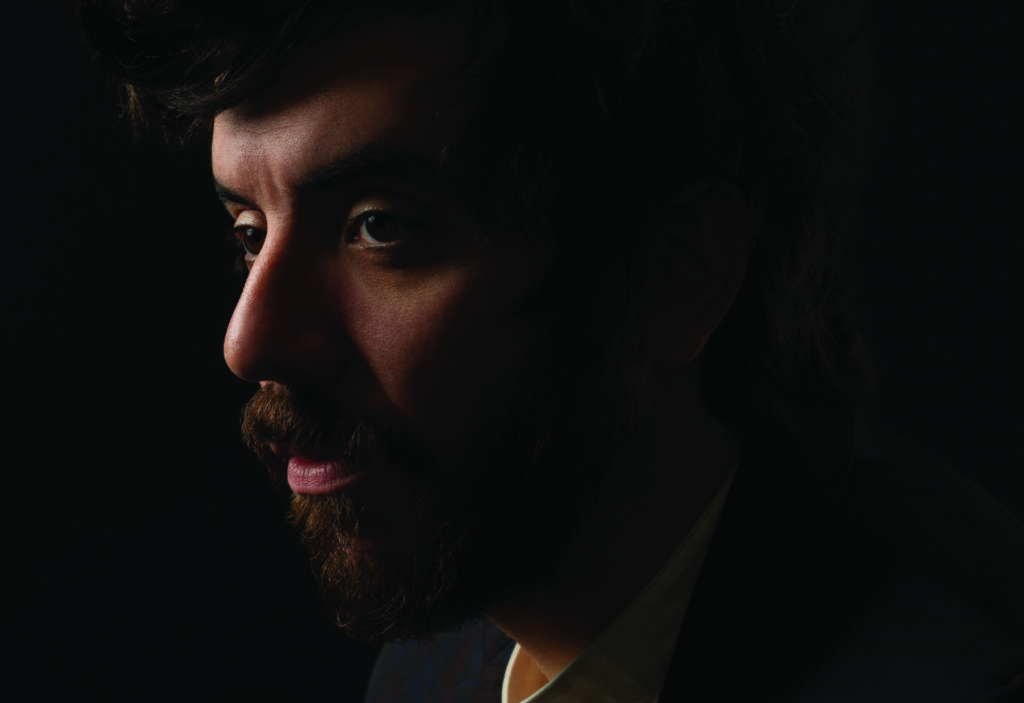 Kaveh Akbar in a suit sitting with a dark background behind him