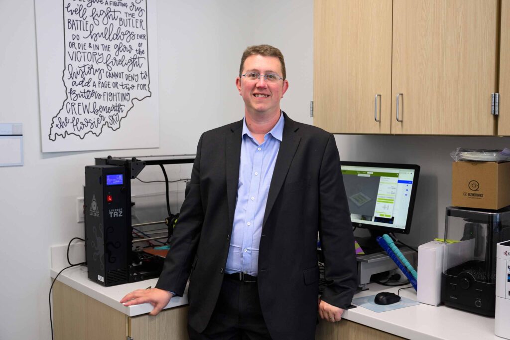 Jeffrey Carvell stands in classroom with engineering equipment behind him.