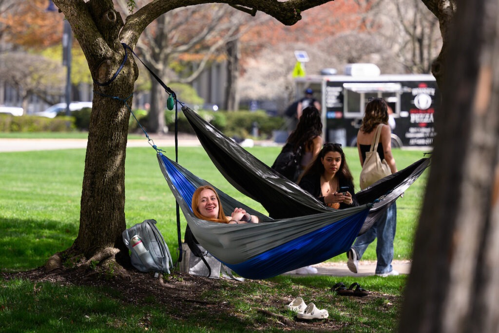 Two students smile and hang in hammocks between two trees on Butler's campus.