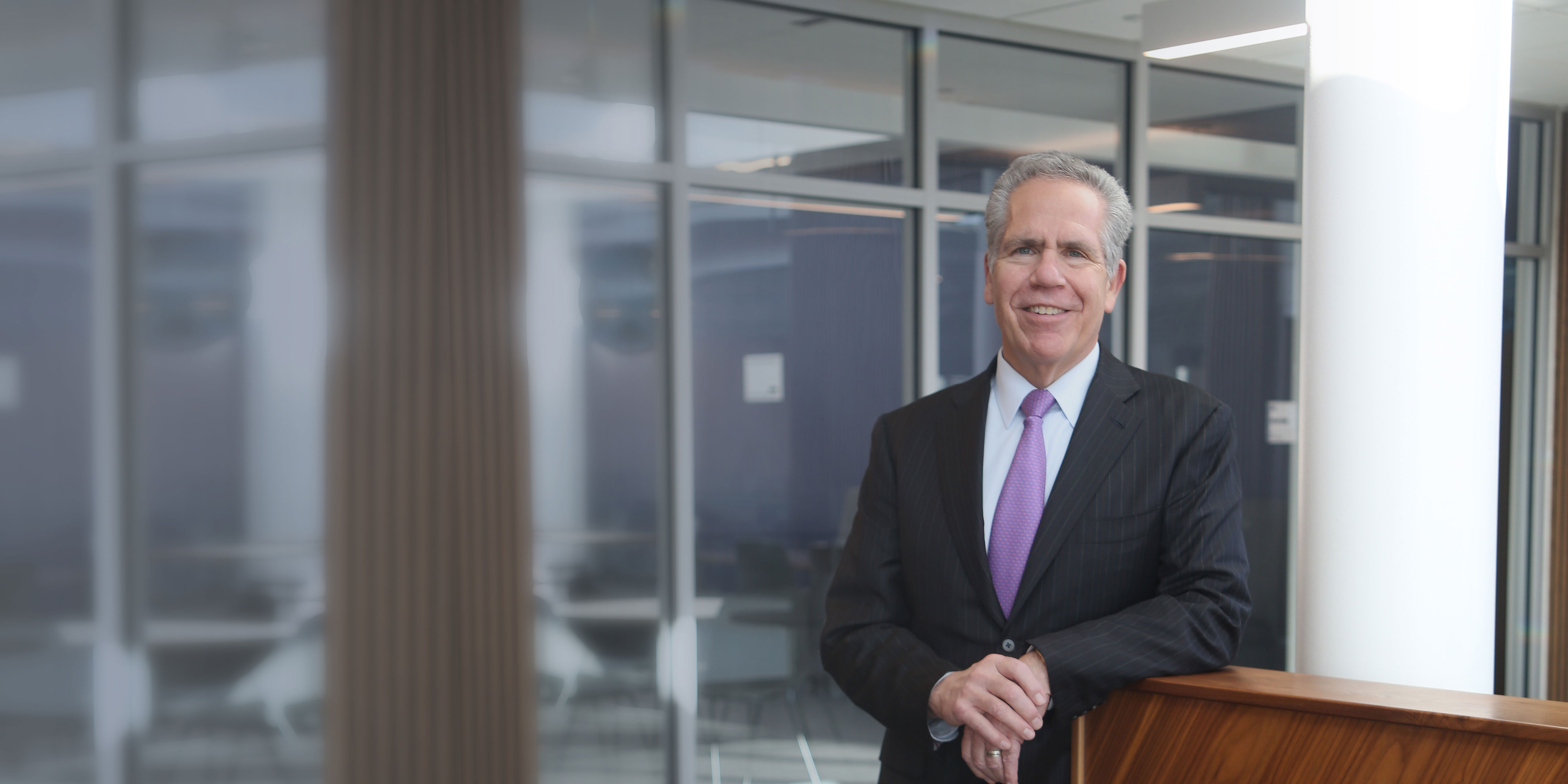 Butler president James danko leaning on a half wall, in gray suit and purple tie