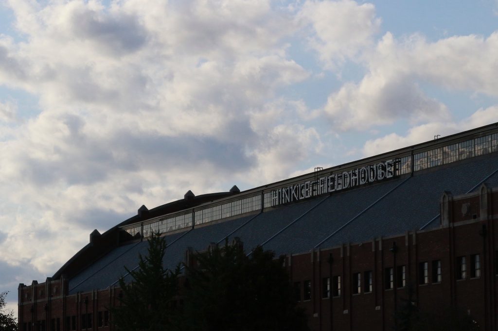 Top of brick arena with words "Hinkle Fieldhouse" and white clouds in the sky above.