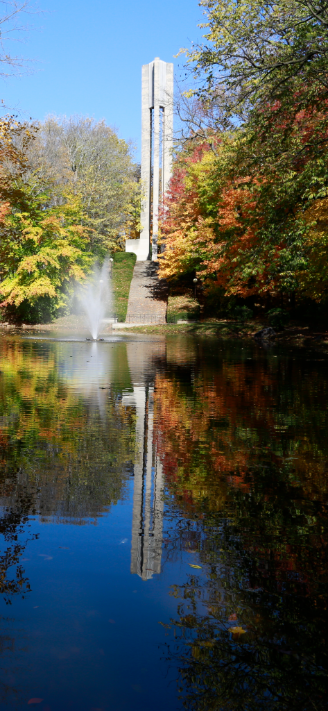 Autumn trees near pond with active fountain and carillon in background.