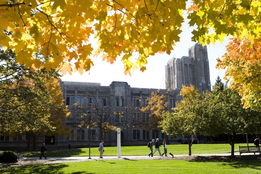 Foreground of yellow leaves on trees, male and female students walking across campus, and the limestone academic building of Jordan Hall in the background.