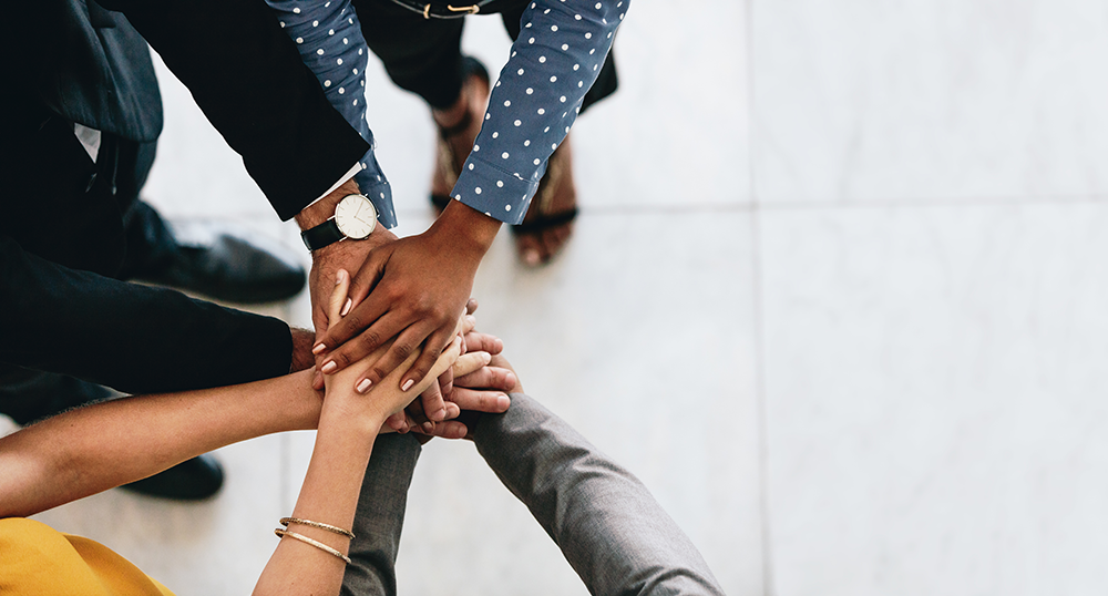 several outstretched arms of various skin tones with hands on top of each other