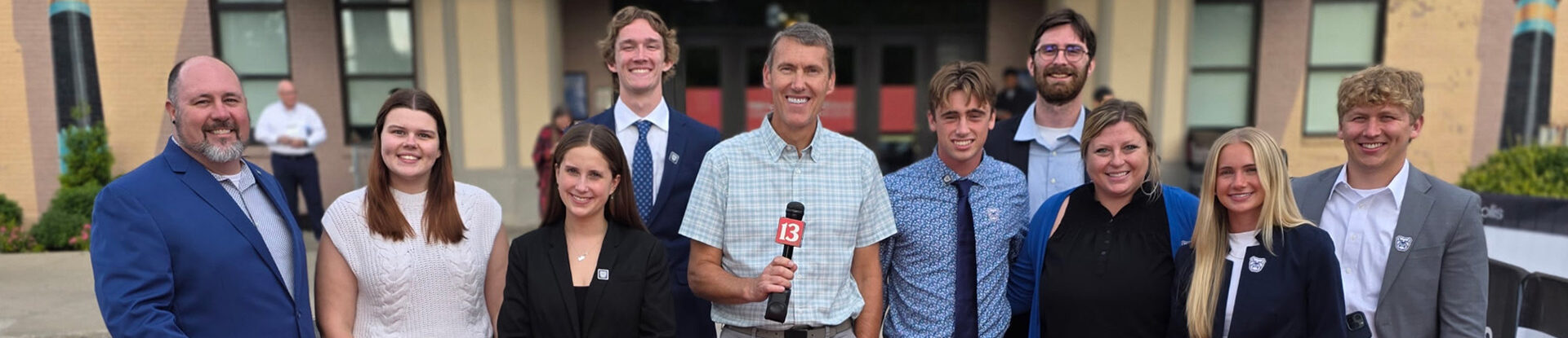 Butler students stand with TV reporter for a group photo outside Old National Center Theatre at the TEDSports Indianapolis event