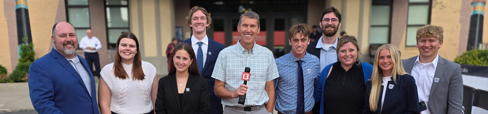 Butler students stand with TV reporter for a group photo outside Old National Center Theatre at the TEDSports Indianapolis event