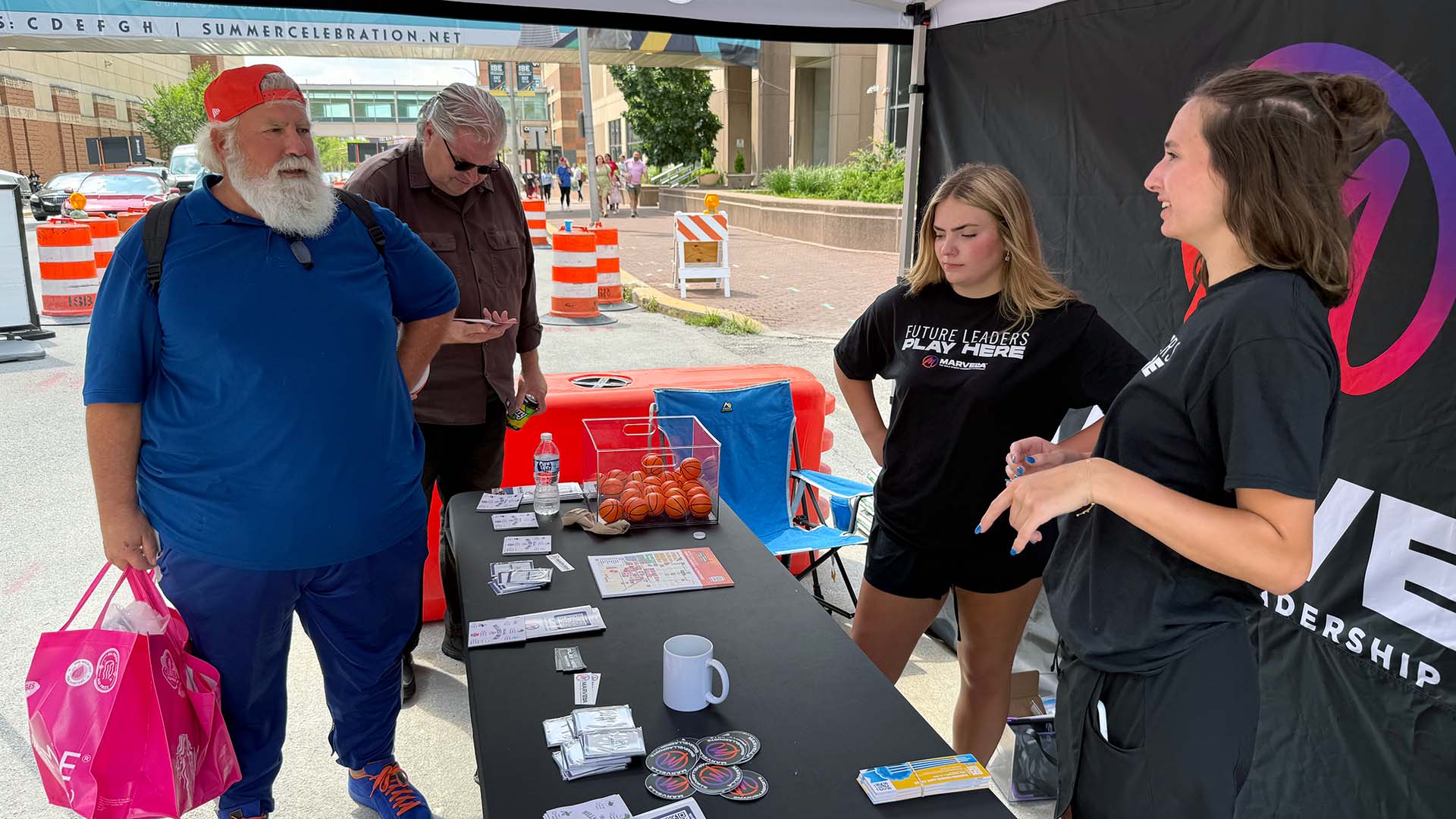 Butler BISE female students speak to two visitors while representing Marvella Mobile at its promotional table during the WNBA All-Star Weekend