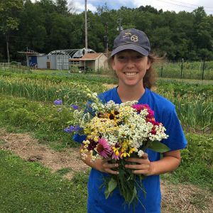 Intern holds bouquet of flowers in front of The Farm at Butler.