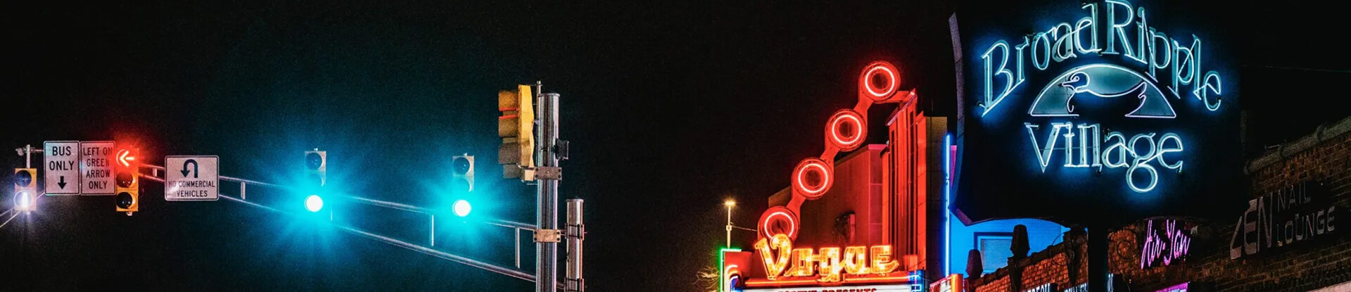 Neon signs and traffic signal lights glow brightly during night street scene in Broad Ripple Village.