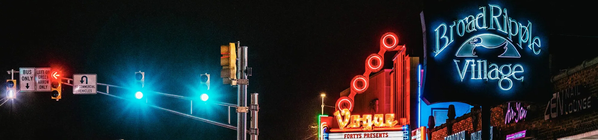 Neon signs and traffic signal lights glow brightly during night street scene in Broad Ripple Village.