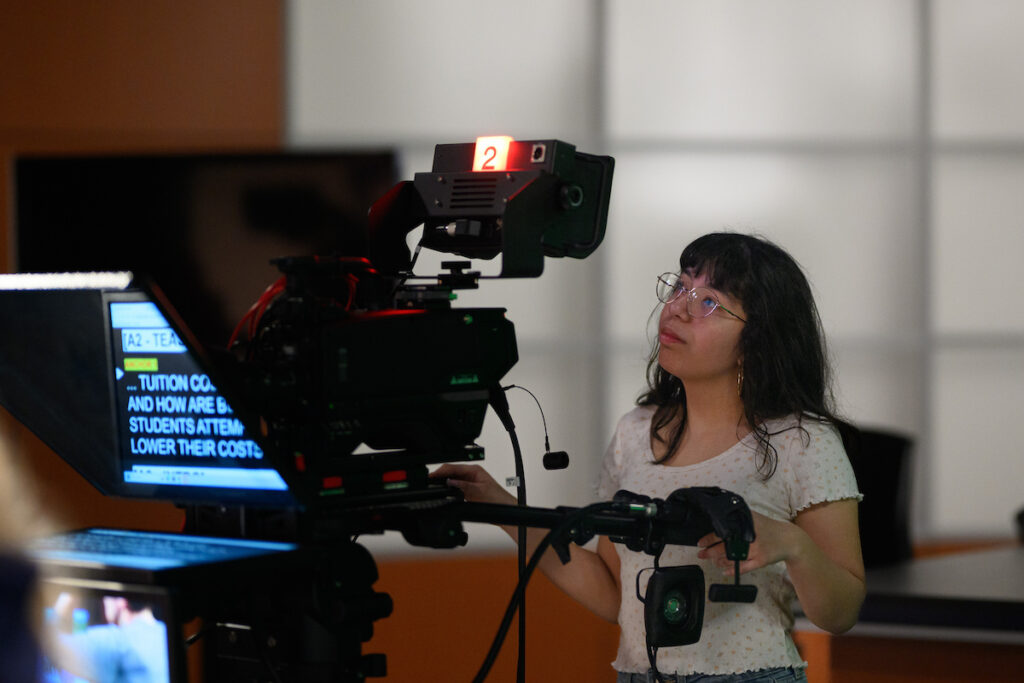 A female Butler student wearing glasses checks on an industry-grade camera for live studio footage. 