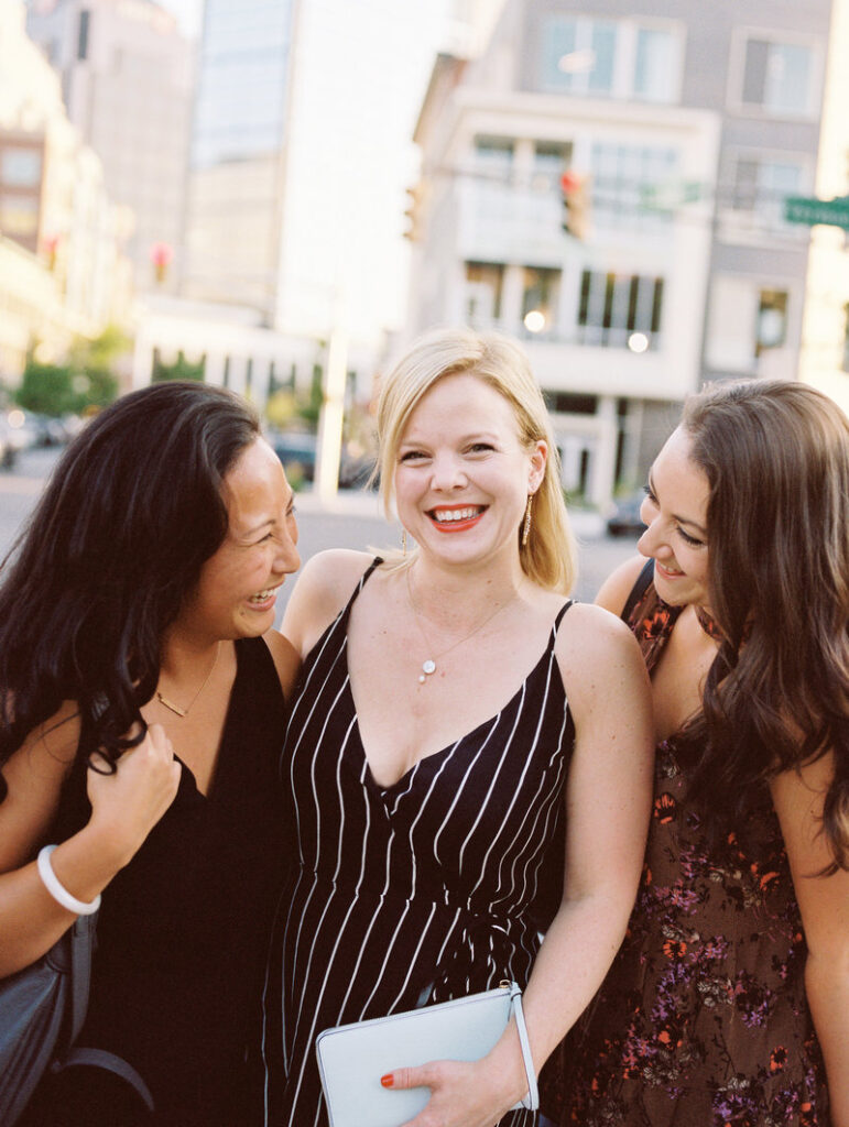 A professional shot of a group of three well-dressed women laughing on a city street.