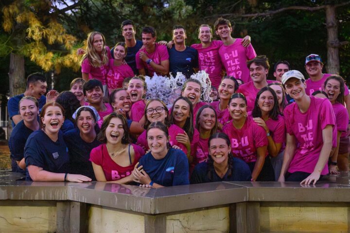 Exuberant group of students pose inside a running fountain while wearing pink shirts.