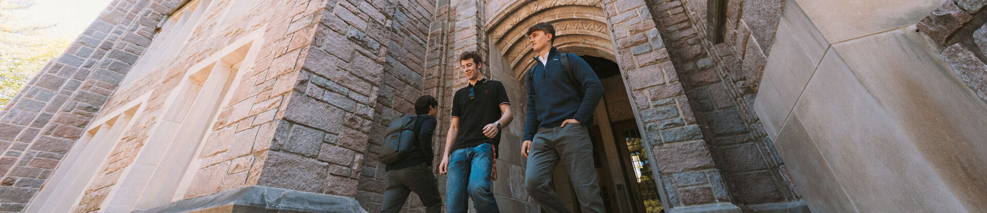 Two male college students exit campus building with limestone archway.