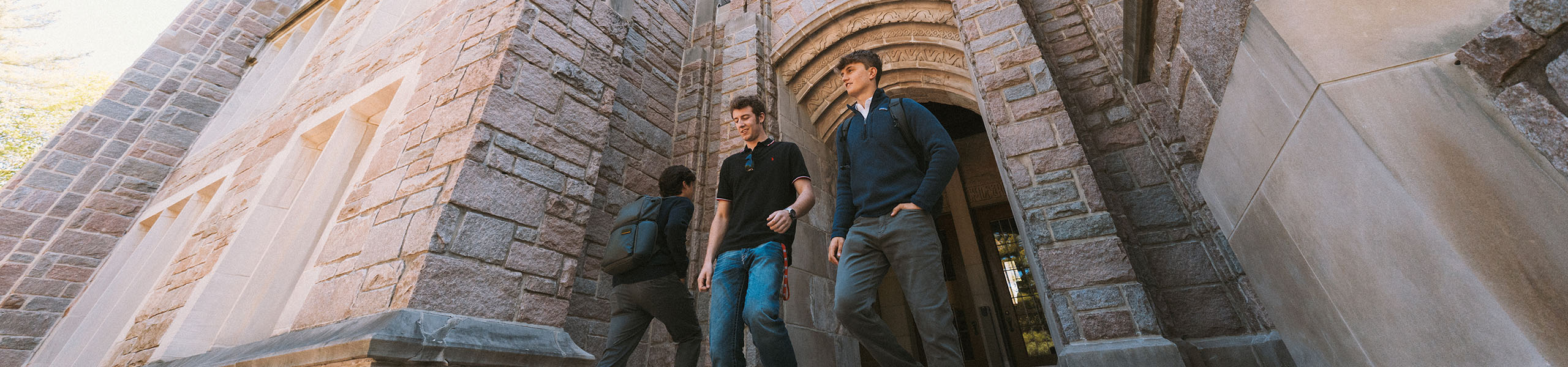 Two male college students exit campus building with limestone archway.