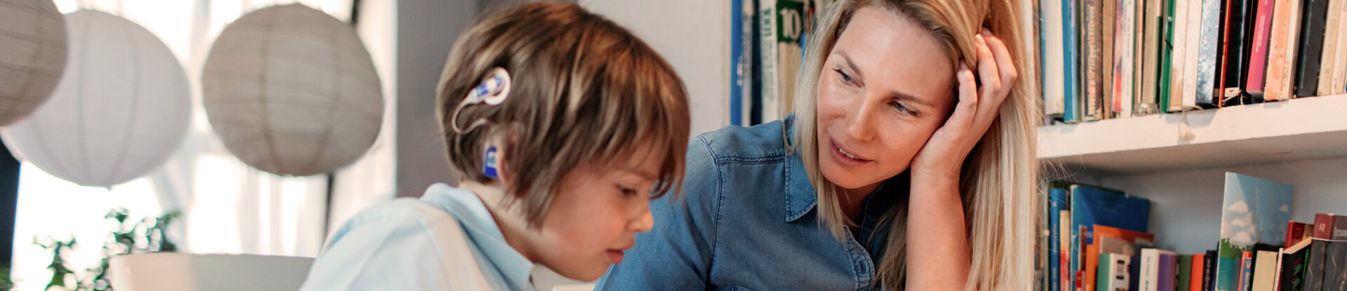 Mother looks at child who is wearing a cochlear implant while helping with school workbook.