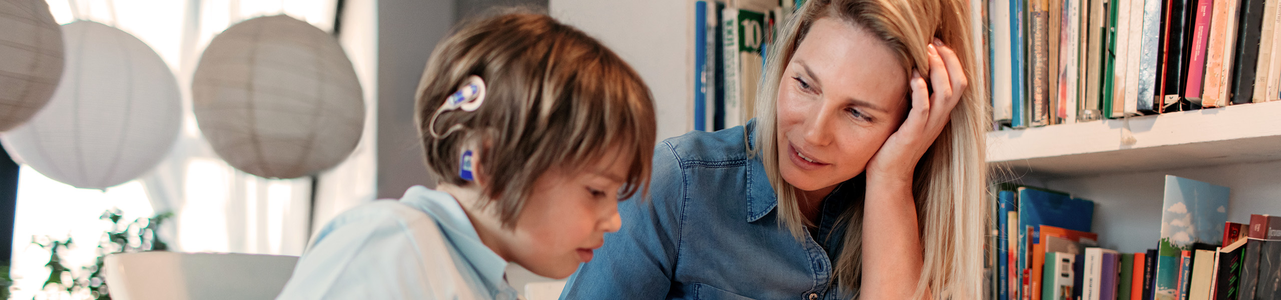 Mother looks at child who is wearing a cochlear implant while helping with school workbook.