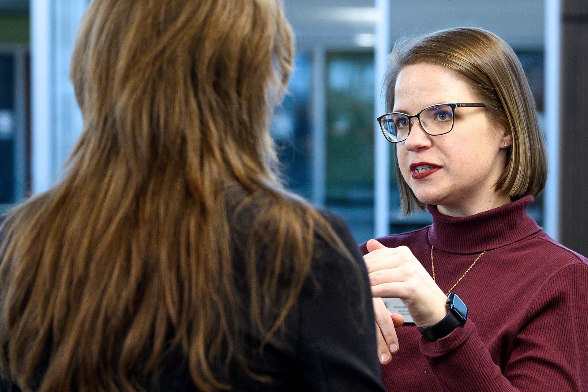 Two female professionals discuss in a bright office setting.