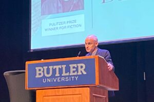 Hernan Diaz reading on stage behind a large wooden podium with Butler University written on it.