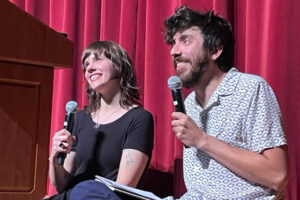 Paige Lewis and Kaveh Akbar smile on stage while holding microphones.