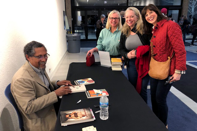 Percival Everett smiles with a group of fans while signing book.