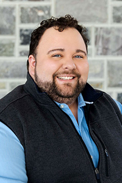 Tony Trimpe smiling in front of stone wall.