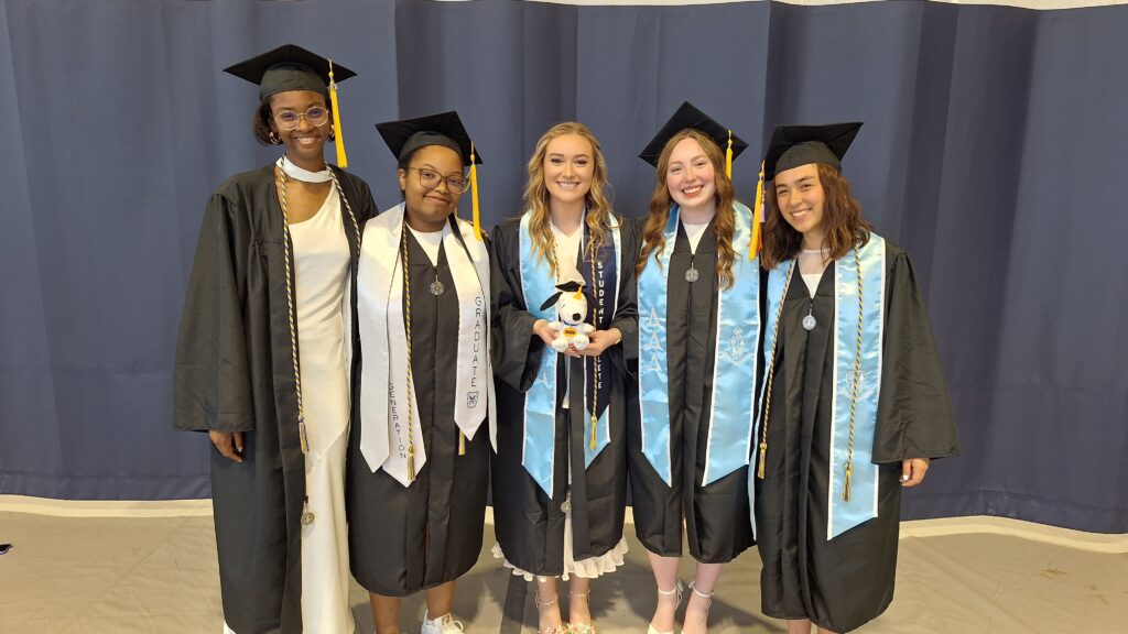 PIcture of 5 CSSE graduates in regalia with a snoopy plush toy