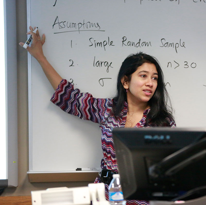 Female professor standing at white board in classroom with a marker in her hands.
