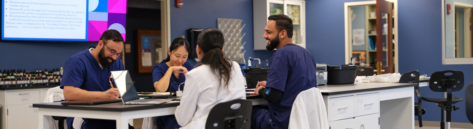 A group of Butler PharmD students in scrubs meet and work in a lab setting.