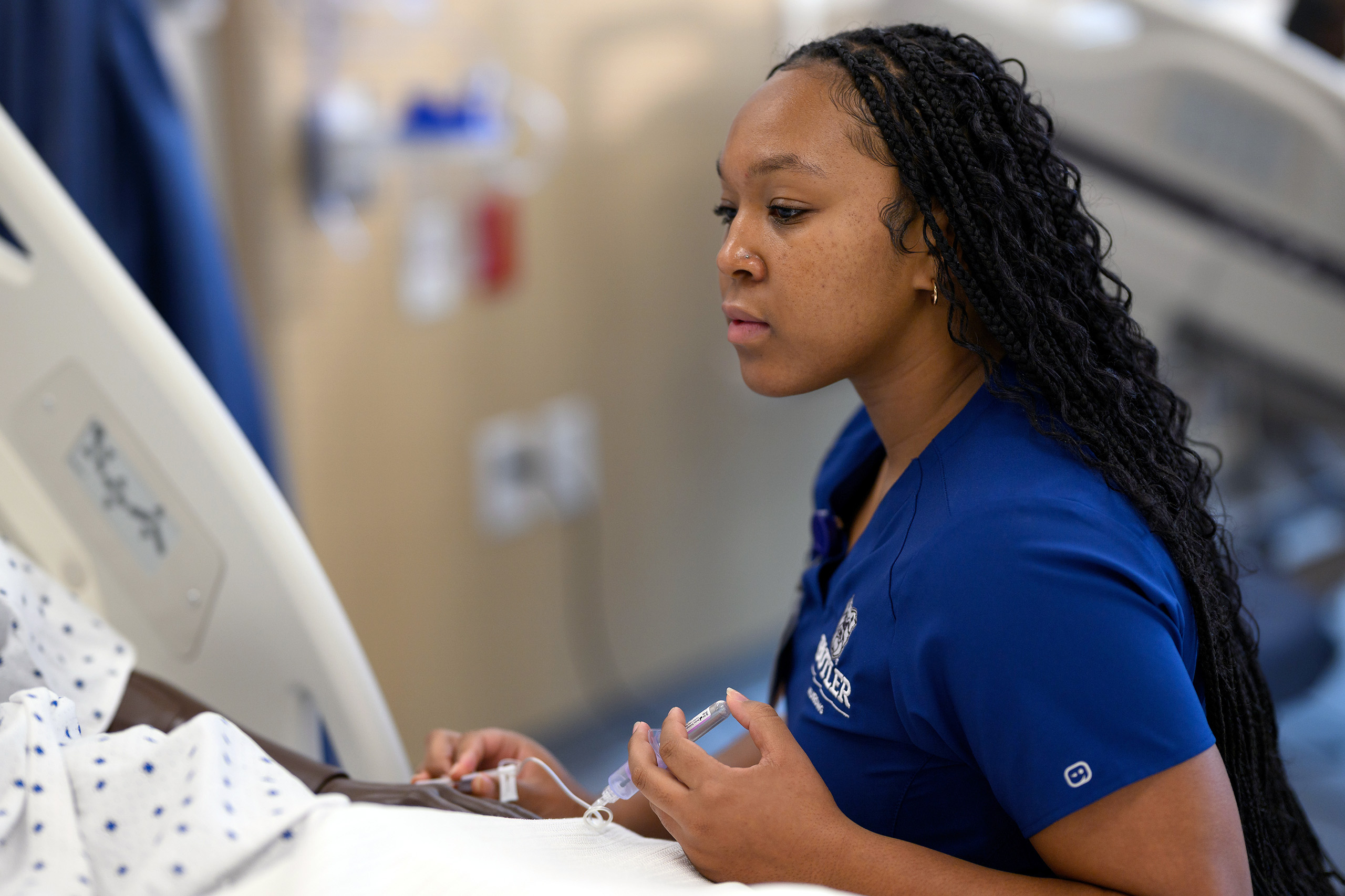 Nursing student administers medicine to the arm of a patient in their clinic bed.