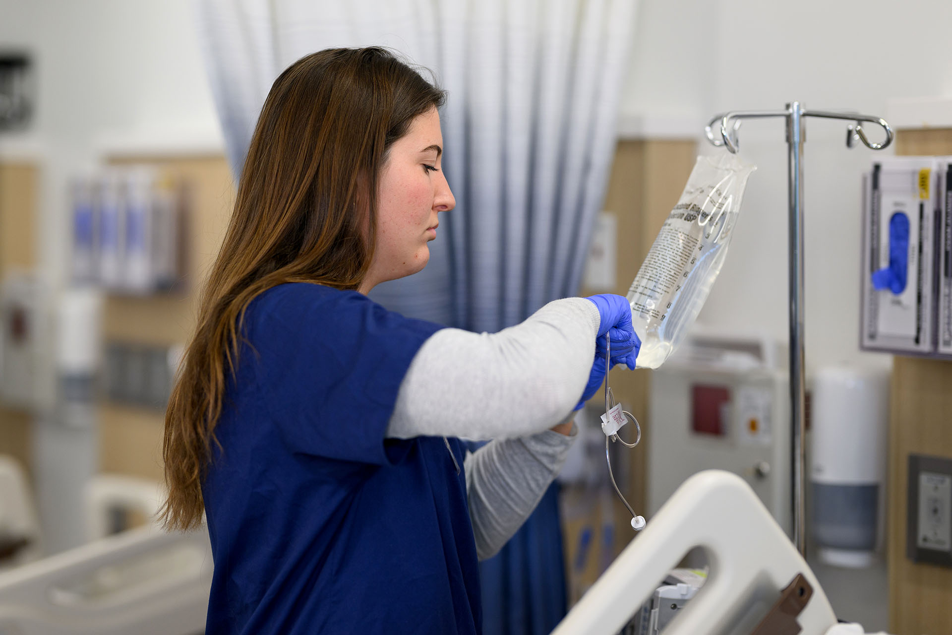 Nursing student connects drip line to saline bag.