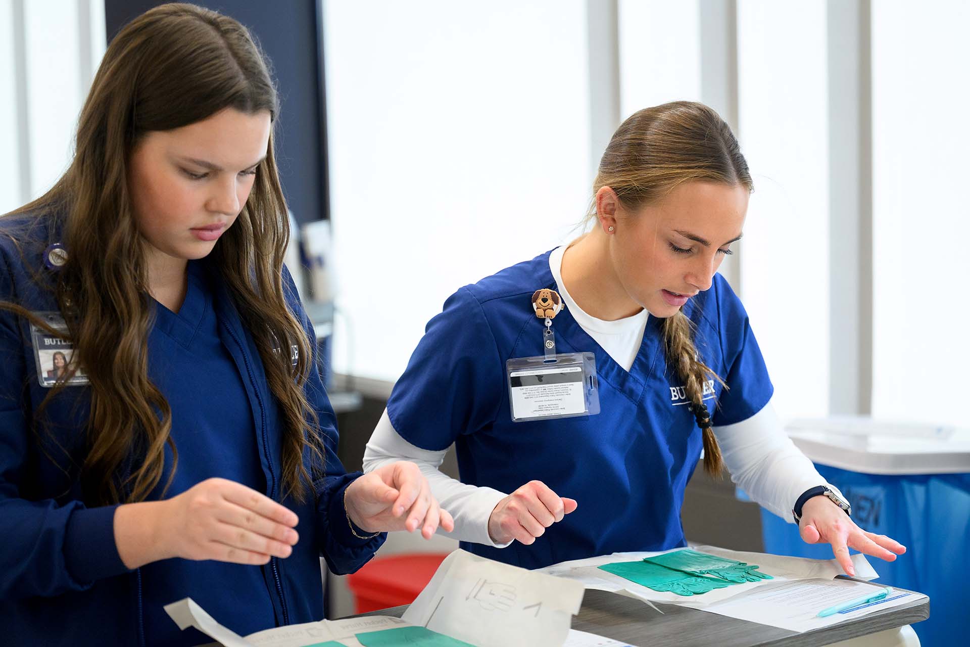 Nursing students read instructions on how to put on gloves.