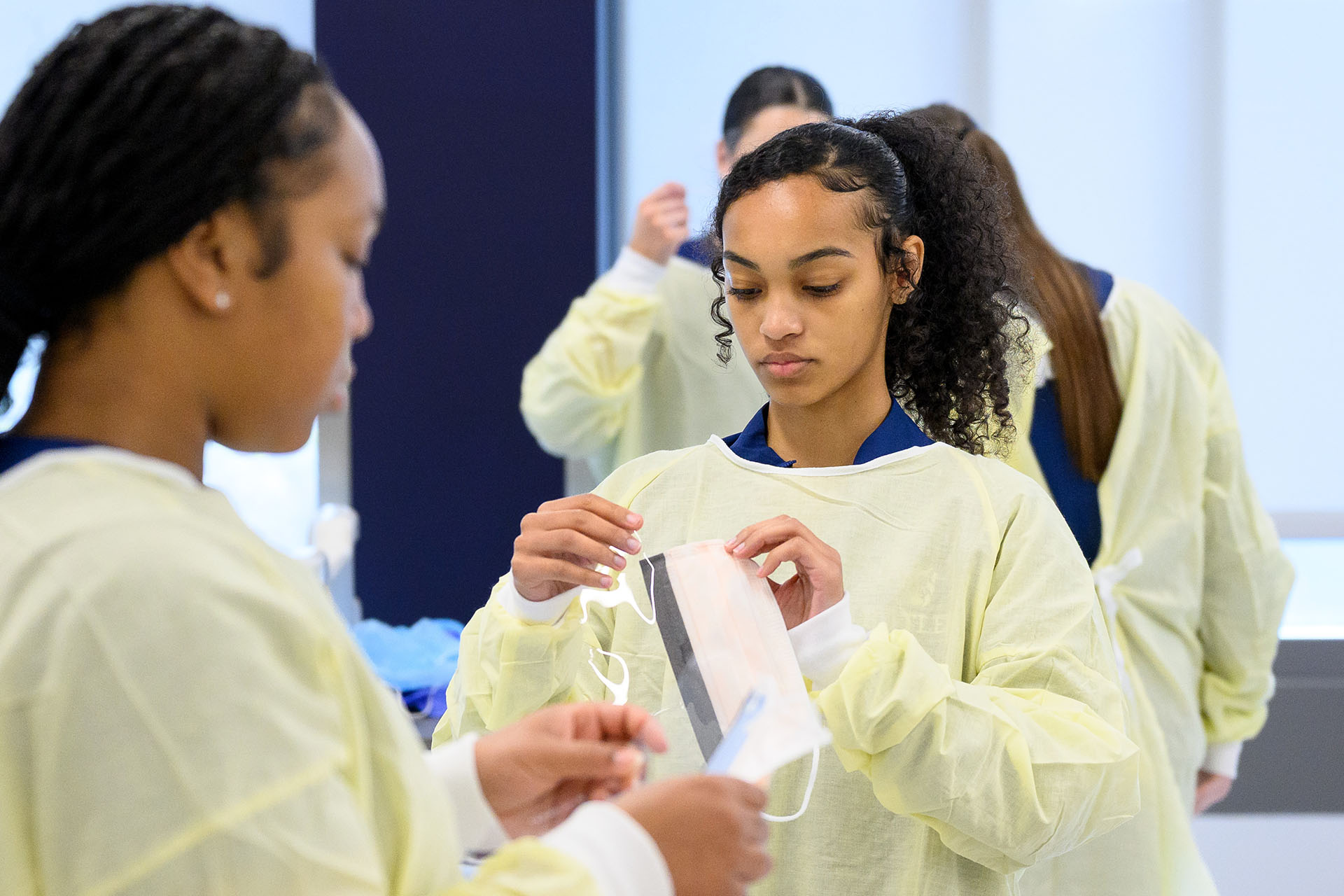 Class of nursing students don yellow gowns and masks.