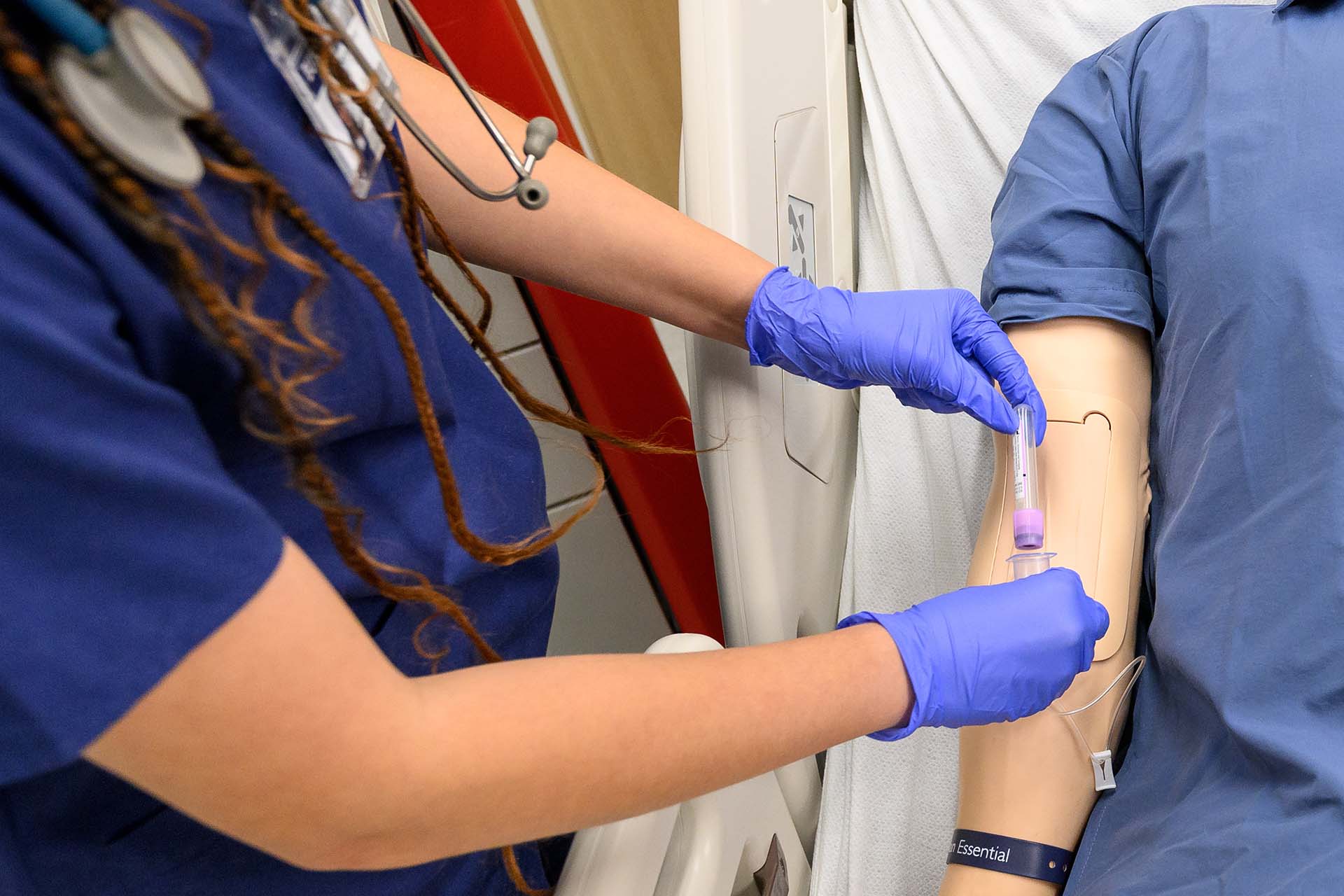 Nursing student holds vial beside manikin patient.
